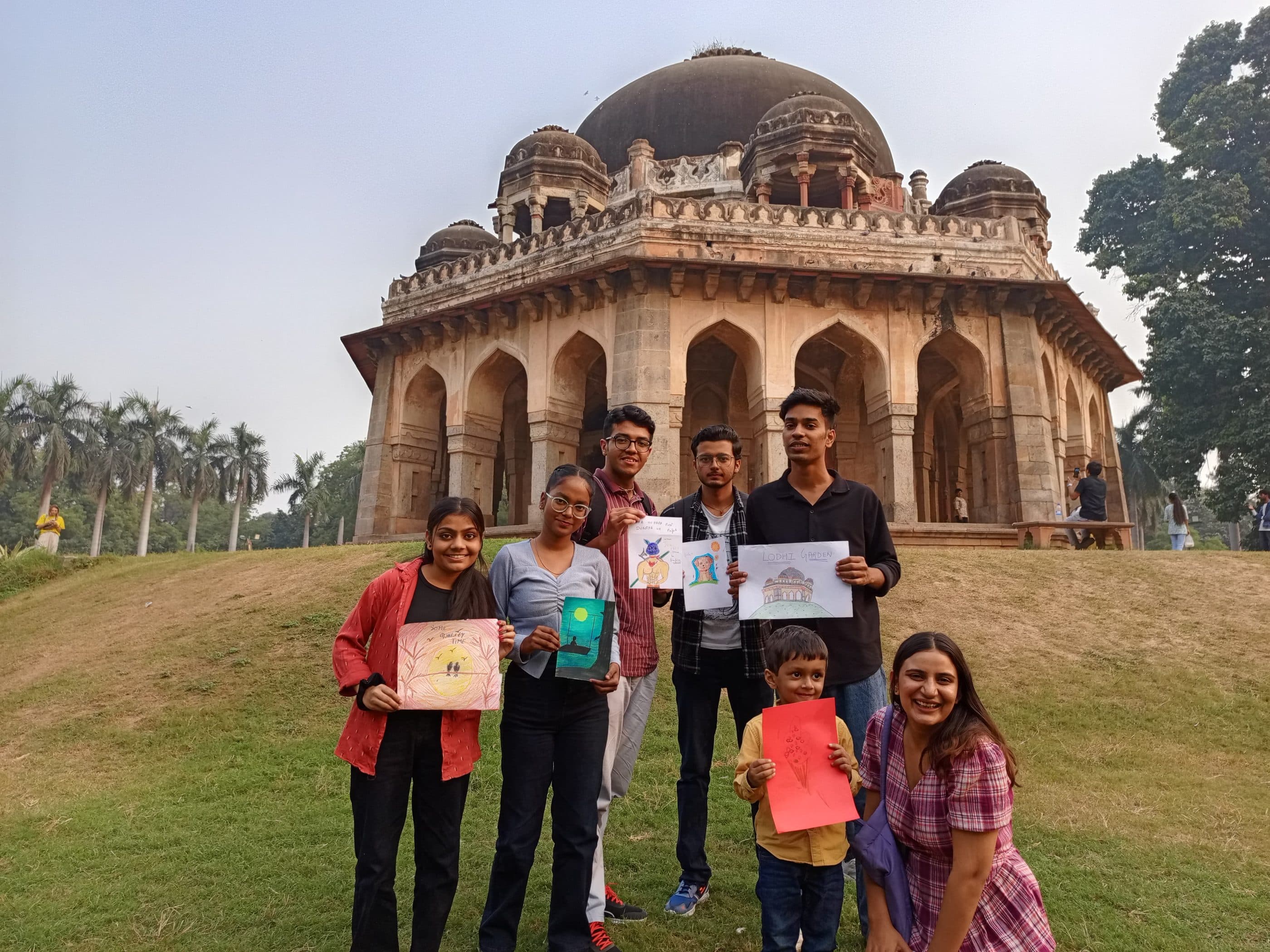 Participants holding their drawings in front of a monument at Lodhi Garden
